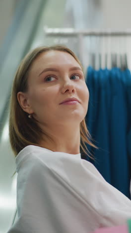 dama mirando estantes de ropa con una cálida sonrisa en una tienda brillante y bien iluminada mira lejos observando algo en el fondo, bolsa de compras cerca de ella