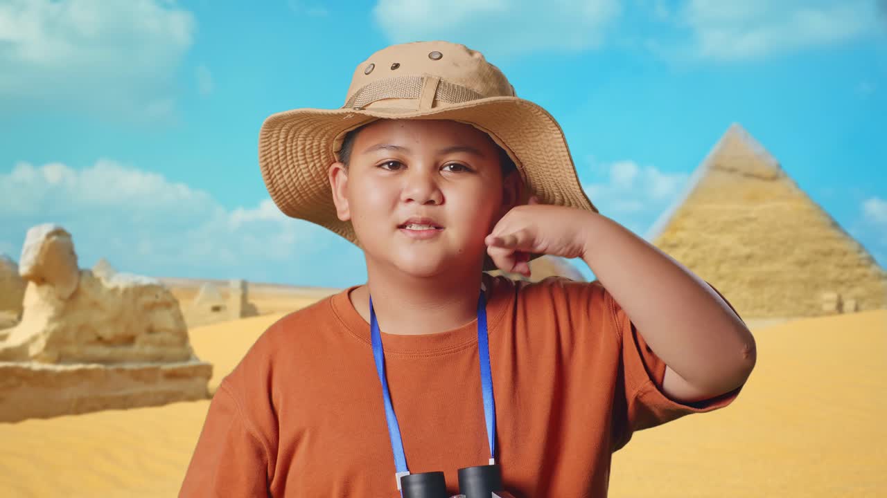 Asian Boy With A Hat And Binoculars Using The Magnifying Glass Then Making Call Me Gesture While Traveling In Giza Pyramid. Boy Researcher Examines Something, Travel Adventure, Close Up
