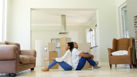 side view of young black couple sitting back to back on the floor in a comfortable home 4k