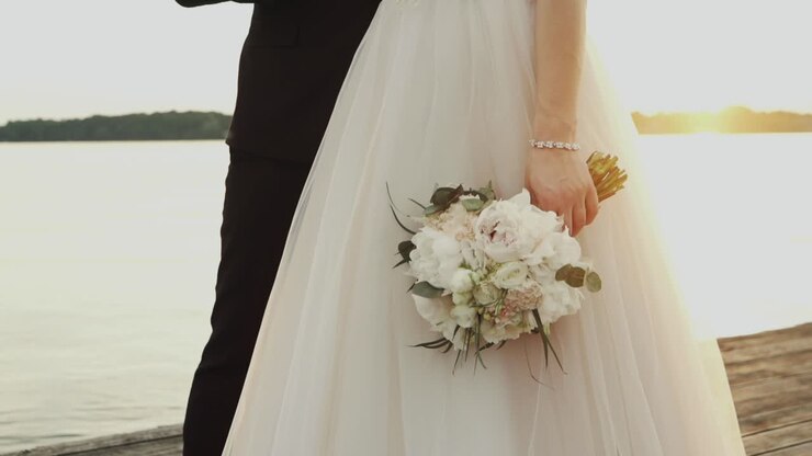 Bride holding a bouquet by the lake during sunset
