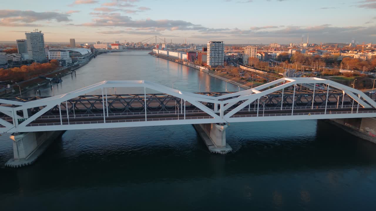Close Aerial Tracking of Rhine Barge: Cargo Ship Sailing under Mannheim Bridge with Sunset Light and Industrial Harbor Infrastructure, Germany