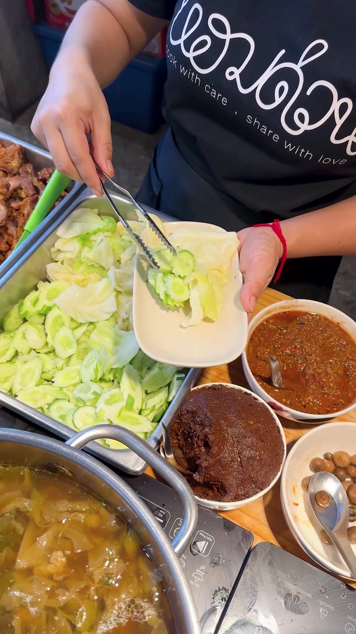 Seorang pedagang kaki lima menggunakan penjepit untuk menyajikan kol dan mentimun segar dengan sambal pedas.