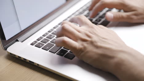primer plano desde la diagonal superior de las manos masculinas escribiendo en las teclas de la computadora portátil