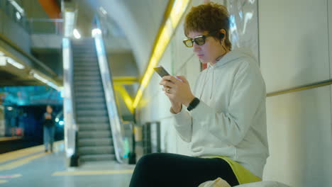 woman sitting on bench in subway and using smartphone