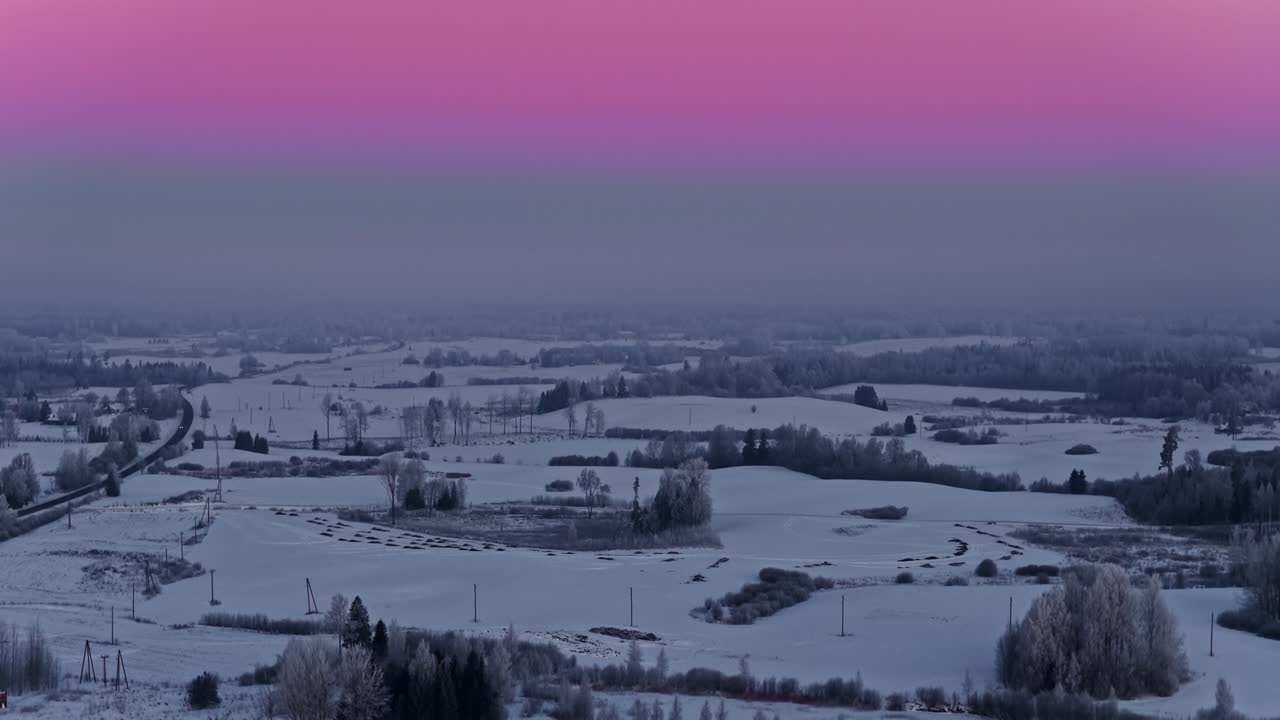 Pastellrosa og lilla himmel over snødekt vinterlandskap, stigende luftfoto.
