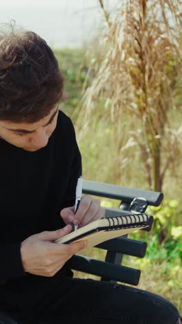 college student writing notes and studying on a bench near the sea