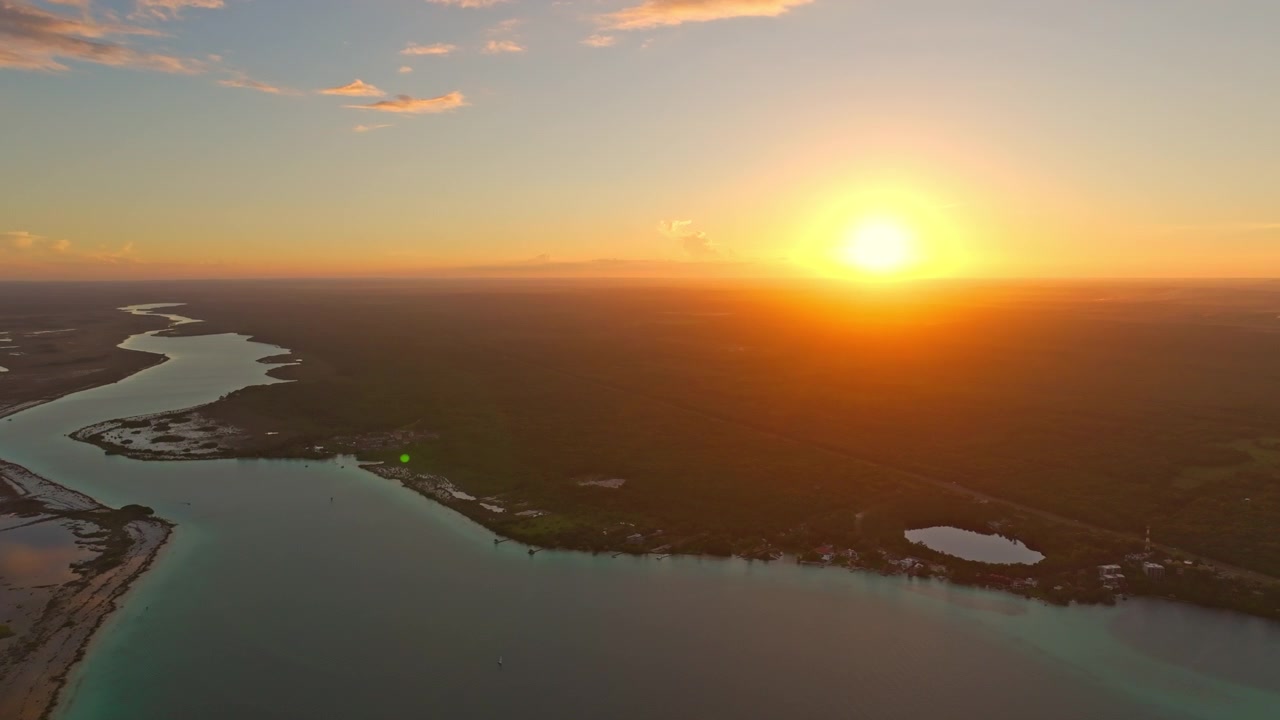Vista aérea ao pôr do sol sobre os manguezais da lagoa de Bacalar, México, com o sol laranja brilhante afundando em direção ao horizonte plano e distante.