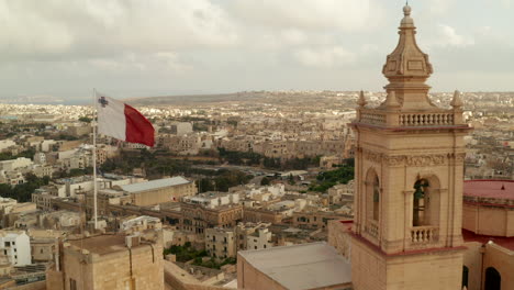 Hermoso-Castillo-De-Arena-De-Gozo-Fuerte-Con-Bandera-De-Malta-Ondeando-Revelando-El-Campo-De-La-Isla-De-Gozo,-Muñeca-Aérea-Delantera