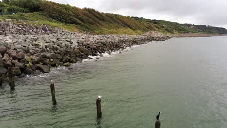 Lush-rocky-North-Wales-hillside-overcast-shoreline-ocean-boulders-aerial-view-dolly-left