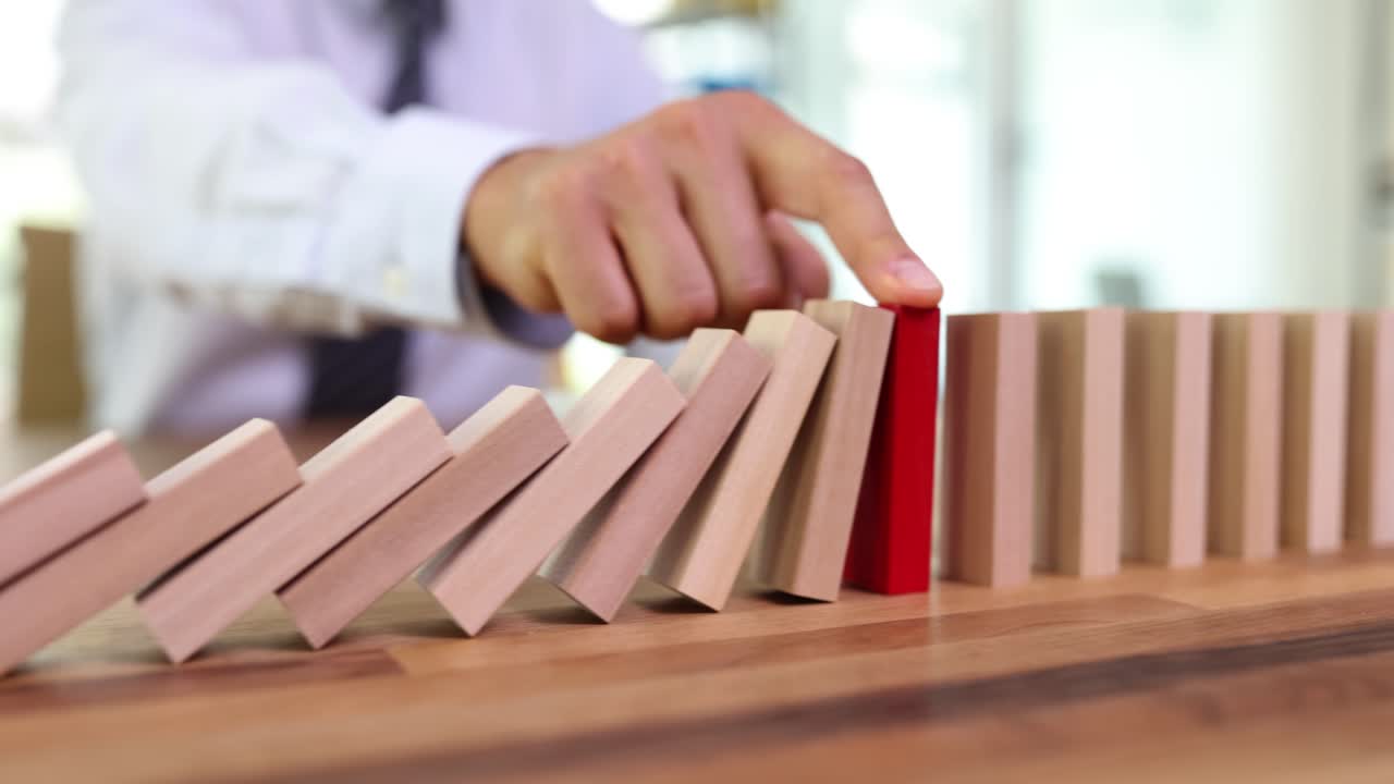 A hand stopping a chain of falling dominoes