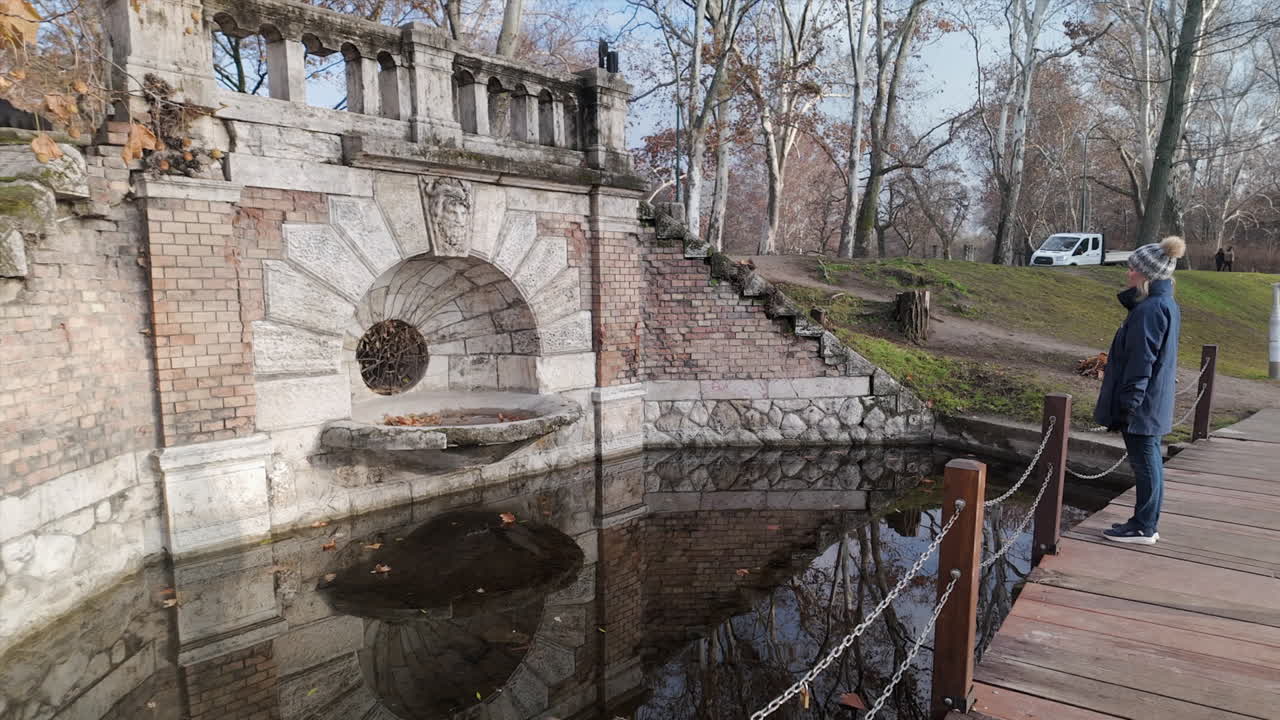 Woman in City Park, Budapest appreciates old fountain and pond, autumn