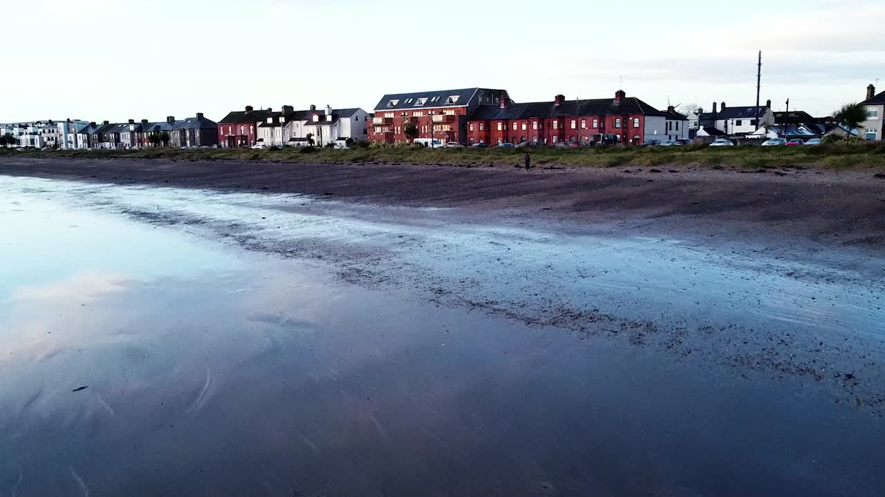 un disparo de dron bajo pasando sobre la costa costera arenosa de la playa de skerries durante la marea baja acercándose a las casas residenciales costeras, irlanda