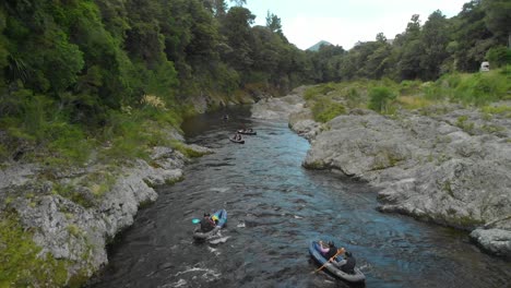 slowmo - kayaking tour paddle boats through canyon on pelorus river, new zealand with native forrest and rock boulders - aerial drone