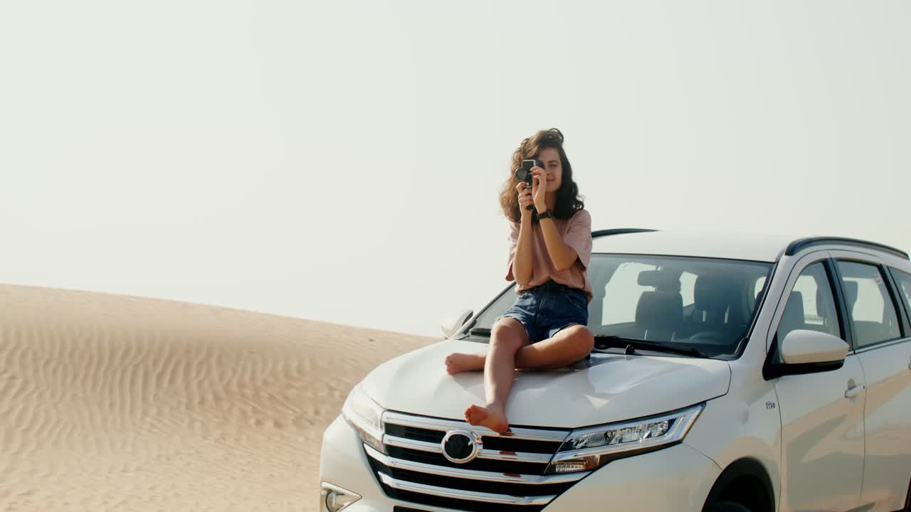 mujer tomando una foto en el desierto en un capó de coche