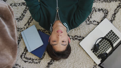 Overhead view of asian boy playing with basketball lying on the floor at home