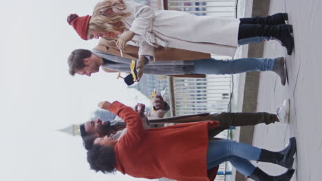 Vertical-video-of-friends-outdoors-wearing-coats-and-scarves-eating-takeaway-fries-on-autumn-or-winter-trip-to-London---shot-in-slow-motion