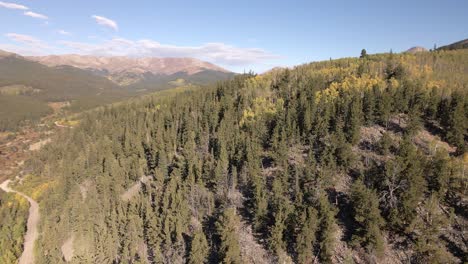 aerial view rotating over a road and aspen covered ridge to reveal distance mountains above treeline