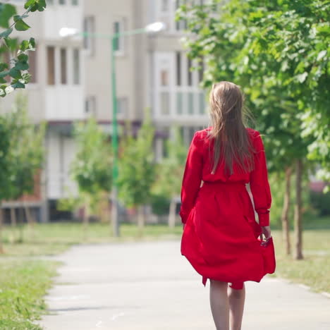 back view of a woman in summer. young female in red dress with long hair is walking on the street to the building in the city.slow motion.