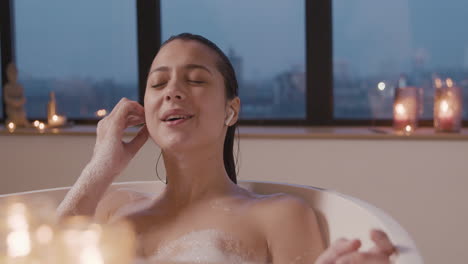 woman putting earphones to listen to music while taking a bath in the bathtub