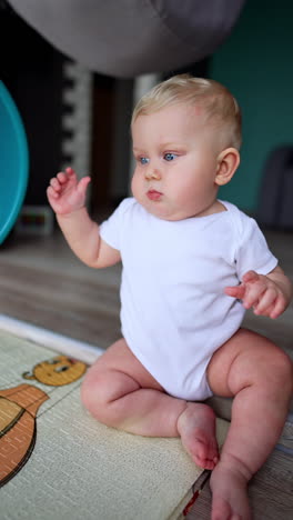 adorable kid wearing white bodysuit sits on the floor. father's hand puts a blue washbowl on son's head. vertical video.