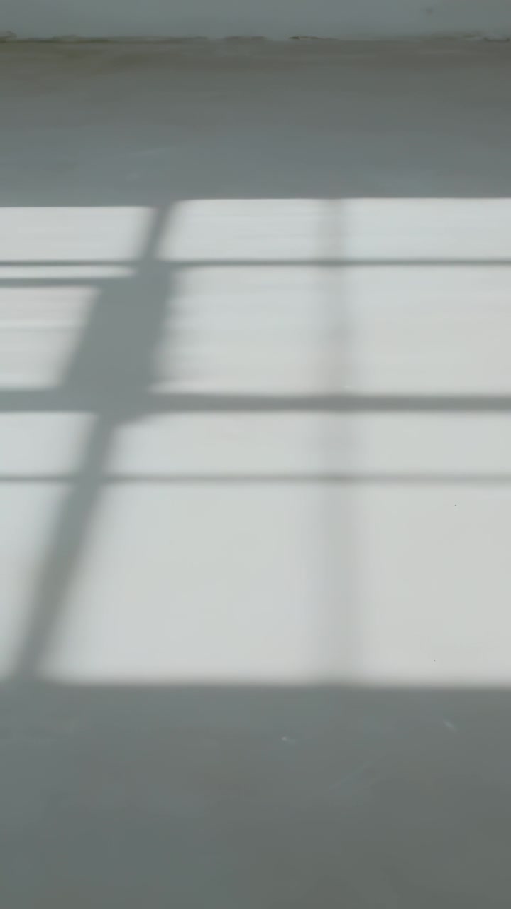 Vertical video: Sliding window-grid shadow shifting across smooth floor, driven by sun movement