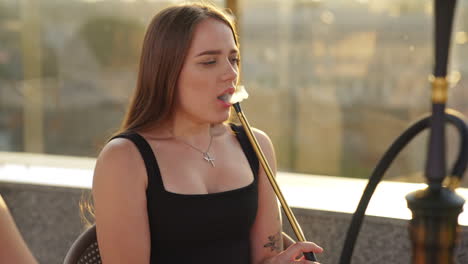 attractive long-haired lady smoking hookah producing much smoke. happy girl friends having good time together at summer vacation.