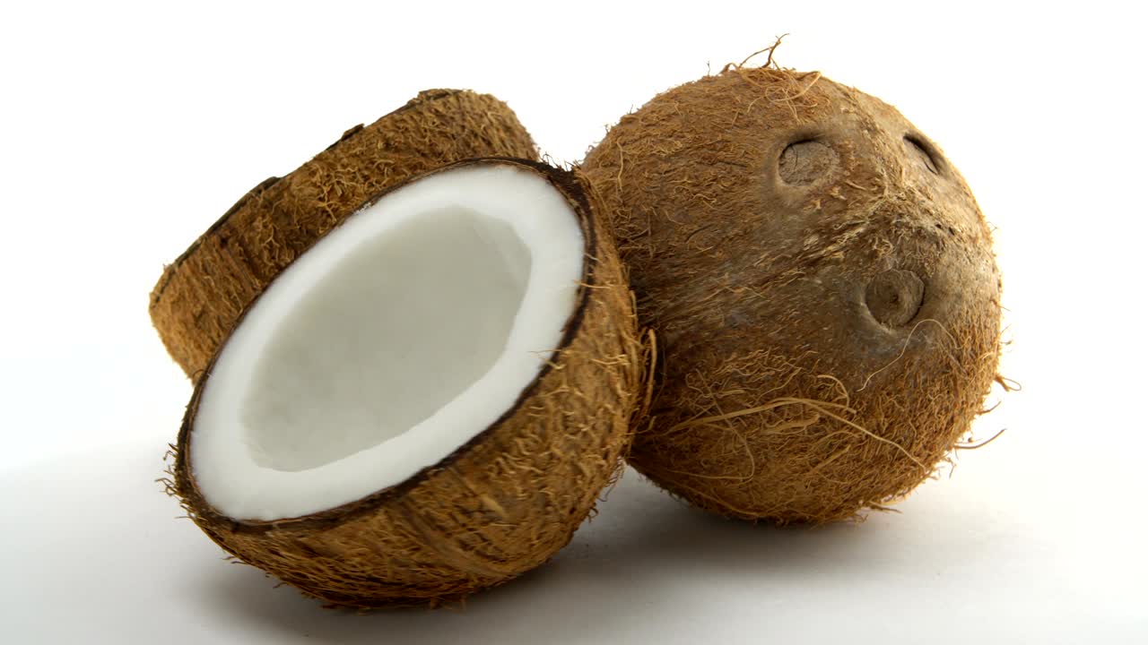 coco tropical maduro y dos mitades de coco girando sobre un fondo blanco. frutas exóticas en bucle