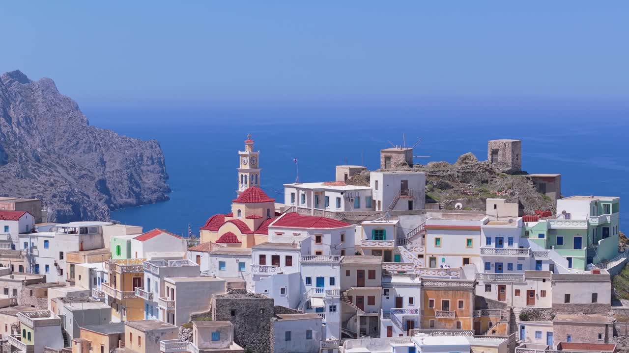 Telephoto drone orbit capturing the colorful traditional village of Olympos in Karpathos, surrounded by a stunning mountainous landscape and Aegean island scenery