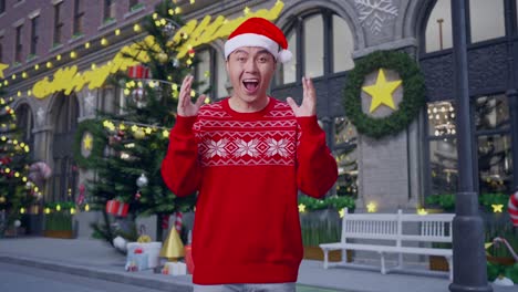 asian man in santa suit showing gesture hands palm, saying wow, and smiling in christmas night