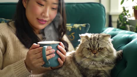 a cozy moment: a woman enjoys a warm drink while relaxing with her content cat in a comfortable living room setting
