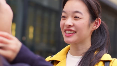 close up of two smiling young female friends meeting and talking in urban setting together