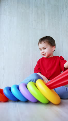 little baby boy turns a colorful pyramid upside down. active caucasian toddler playing with a toy at home. vertical video.