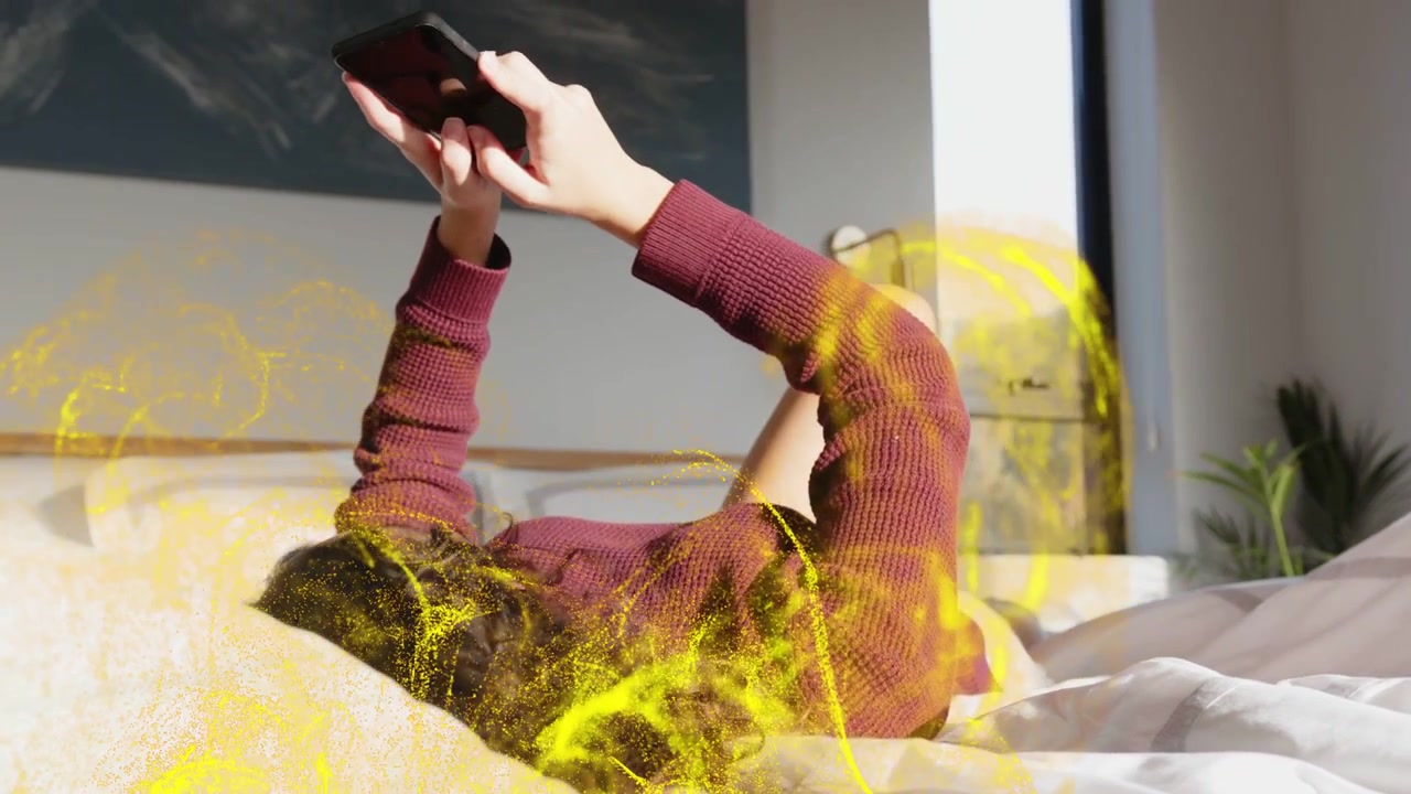 Liggende kvinde tapper på telefonen i sengen, vipper den og får guldpartikler til at hvirvle rundt om kroppen, mens hun tester AR.