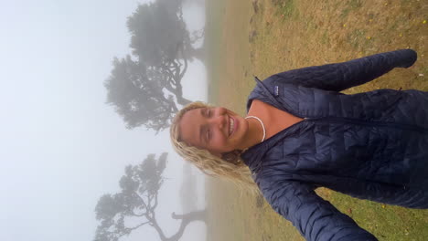 beautiful blonde girl with a smile on her face filming herself while walking lost in a mystical misty forest