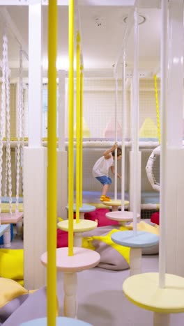 a young child carefully navigating a colorful indoor playground with soft, hanging platforms, focusing on balance and coordination