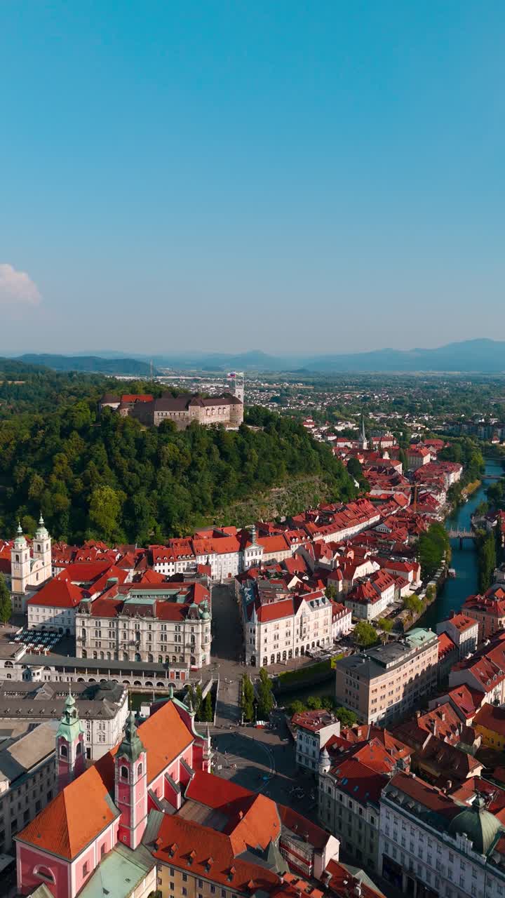 Sorvolo orbitale verticale con drone sulla città vecchia di Lubiana al tramonto, che rivela il castello in cima alla collina, il Triplice Ponte, Piazza Prešeren e il tortuoso fiume Ljubljanica.