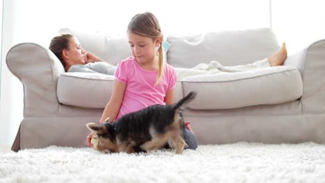 Niña-Jugando-Con-Cachorro-Y-Hueso-Con-Su-Madre-Leyendo-En-El-Sofá.