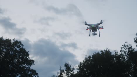 un dron volando frente a algunos árboles a través del cielo azul nublado