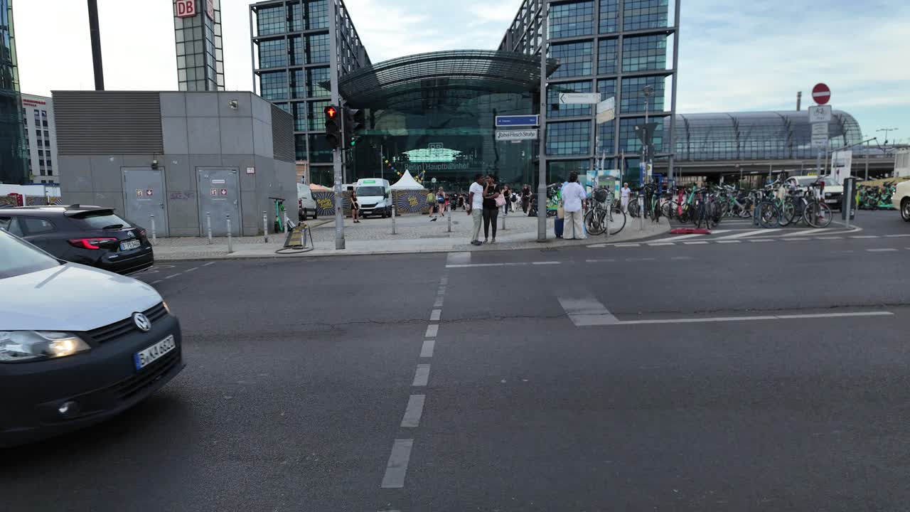 Outside Berlin Central Station showing commuters, bicycles, and modern architecture under a blue sky. Tilt Up