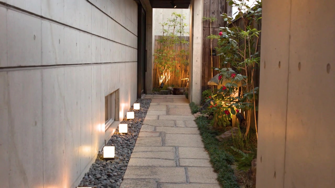 Un sentiero in pietra tra muri di cemento presenta lanterne a cubo luminose e bambù a Kyoto, Giappone