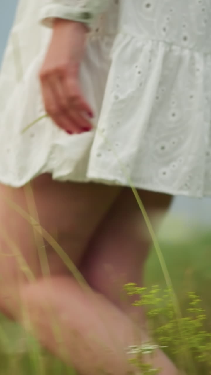 은  드레스를 입고 울창한 초록색 을 걸어가는 여성의 하부 몸의 클로즈업. 그녀의 손은 구슬로 장식된 드레스의 을 부드럽게 들고 있습니다.