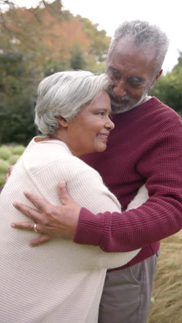 vertical video of senior biracial couple embracing and smiling in garden, unaltered, in slow motion