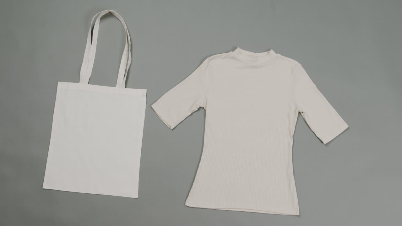 primer plano de una bolsa blanca y una camiseta sobre un fondo gris, con espacio de copia, cámara lenta