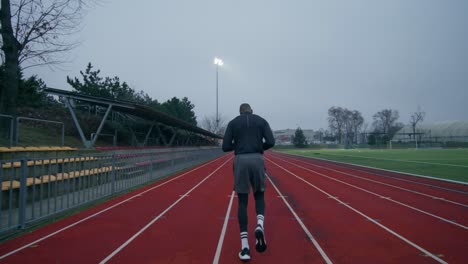 man running on a track in a cloudy stadium