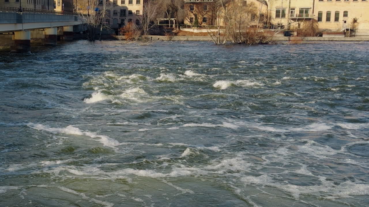 Ripresa con carrellata lenta delle rapide correnti del fiume Fox che scorrono verso valle con vecchie cartiere storiche sullo sfondo, Appleton, Wisconsin, di giorno