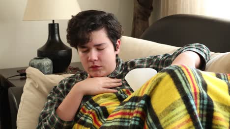 sick teenage boy lying on sofa at home and coughing