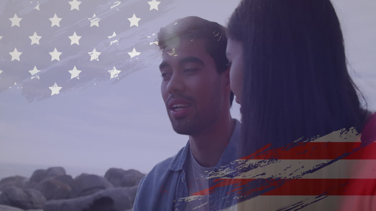 animación del efecto de la bandera de los ee.uu. contra una pareja biracial hablando entre sí en la playa