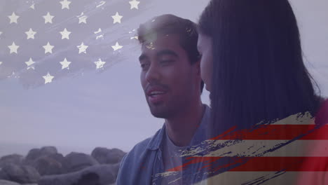 animación del efecto de la bandera de los ee.uu. contra una pareja biracial hablando entre sí en la playa
