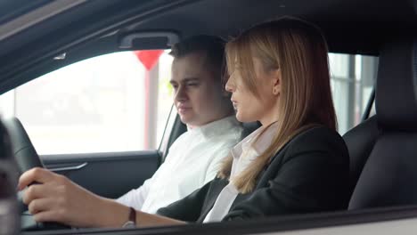 stylish man sitting in car salon and talking with female car dealer. professional helping client to choose best automobile in showroom