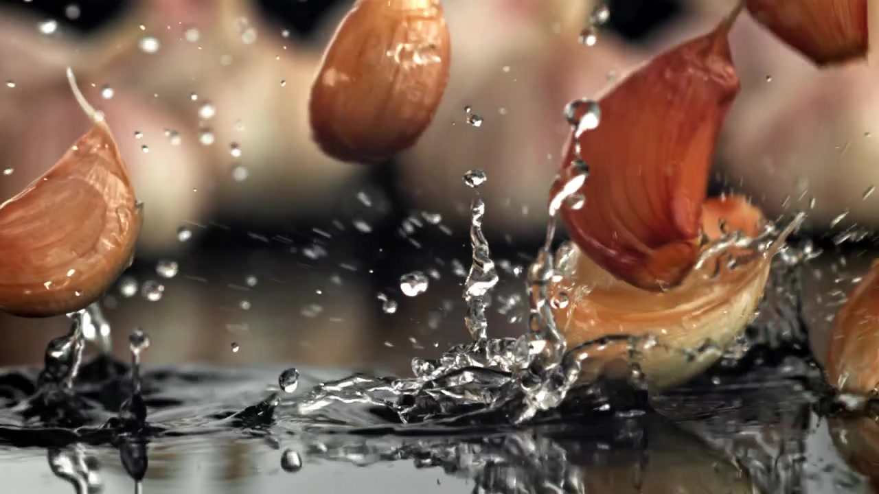 Spicchi d'aglio freschi che cadono nell'acqua con schizzi al rallentatore.
